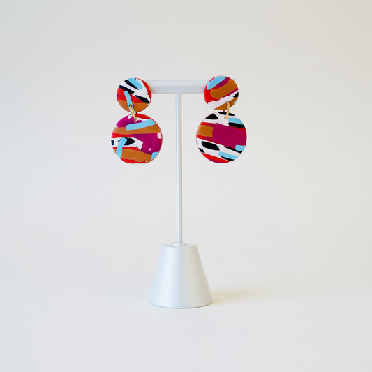 Colorful circular earrings on a white stand against a white background